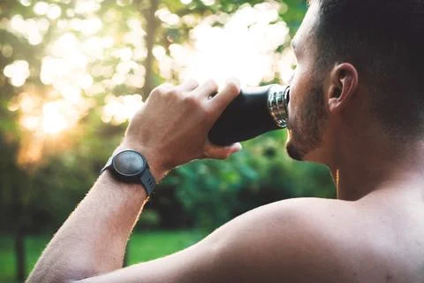 Over the shoulder view, man drinking water outside, wearing a smart watch on the Stock Photos