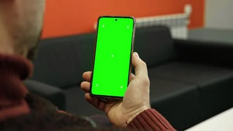Over the shoulder view of man holding smartphone vertically with green scre.. Stock-Fotos