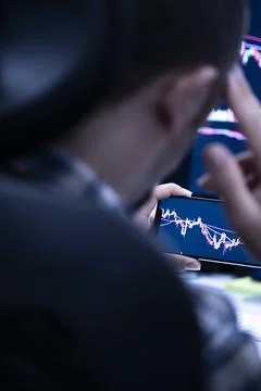 Over-shoulder view of a man holding a phone with candlestick chart Stock Photos