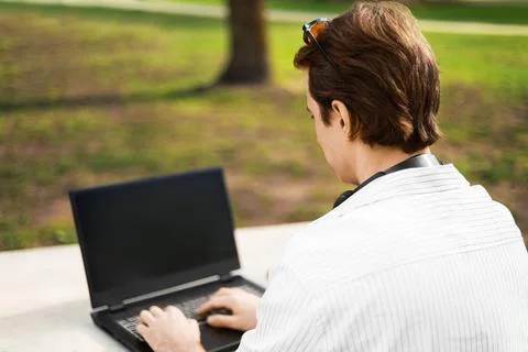 Over-the-shoulder view of a man typing on a laptop while working outdoors i.. Stock Photos