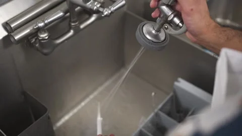 Over-shoulder view of man using spray nozzle to clean baking tools in sink Stock Footage 317221761