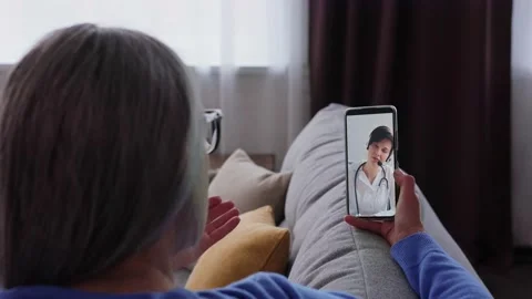 Over shoulder view of sick senior woman patient at home using smartphone for 스톡 동영상 196168864