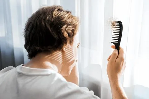 Over shoulder view of a stressed man looking down at a comb full of lost ha.. Fotos Stock