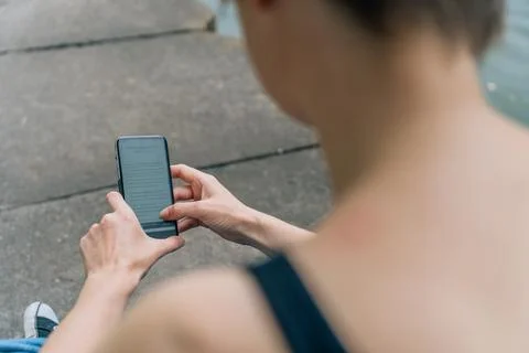 Over-shoulder view of woman using smartphone on concrete riverbank Stock Photos
