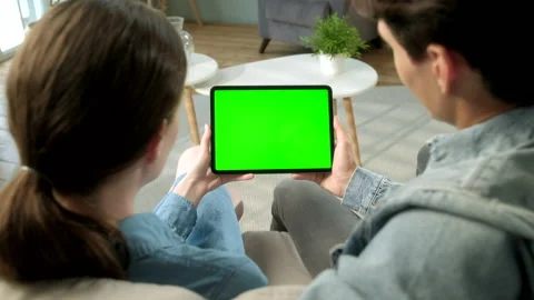 Over The Shoulder View Young Couple at Home Sitting on a Sofa Using with Green Vídeos de archivo 133285216