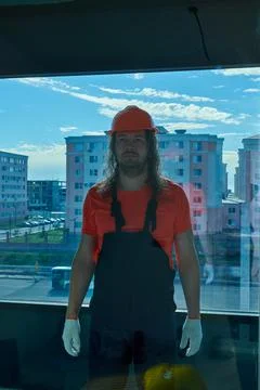 In overalls a builder in a helmet makes a face behind the glass Stock Photos