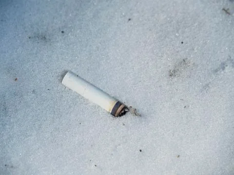 An overbought cigarette butt with a white filter lies in white snow. Stock Photos