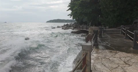 On an overcast day, rough waves spray a tree lined stone coastal path. Stock Footage 316880058