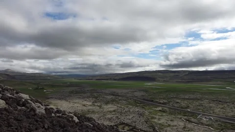 Overcast sky with fast moving clouds casting shadows over a vast volcanic valley Stock Footage 346325703