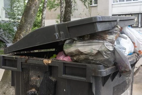 Overfilled garbage bin with plastic bags on city street conceptualizing mun.. Stock Photos