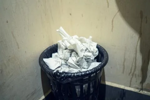 Overfilled plastic bin with gray low-quality toilet paper in public restroo.. Stock Photos