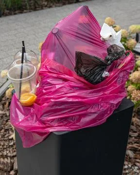 Overflowing garbage bin with plastic cups and trash on street Stockfoto's