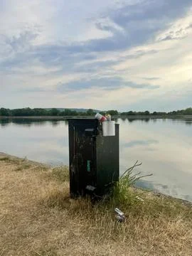 Overflowing Trash Bin by Lakeside on a Cloudy Day – Environmental Contrast Stock Photos