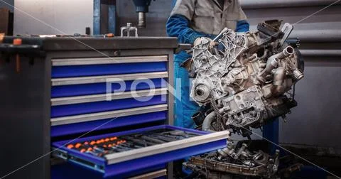 Overhaul repair. The young auto mechanic dismantles the opposing engine for Stock Photos