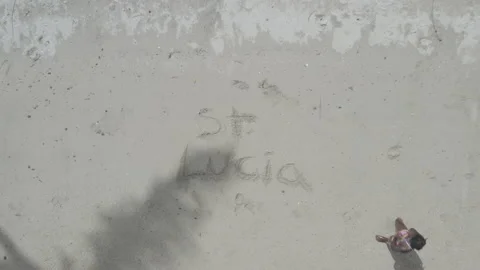 Overhead aerial pulls up over "St. Lucia" in the sand on a beach in Marigot Bay Vídeos de archivo 209426441
