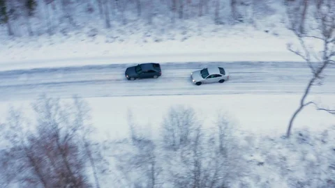 Overhead aerial tracking shot of two cars drifting and racing on snowy road Stock Footage 100732770