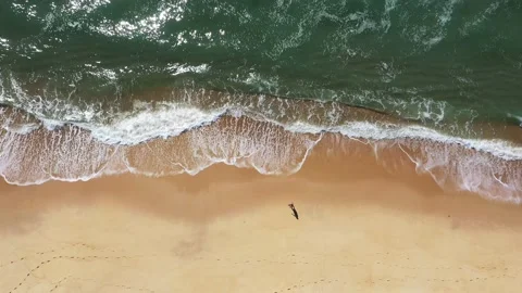 Overhead aerial view of a man walking alone on empty beach Stock Footage
