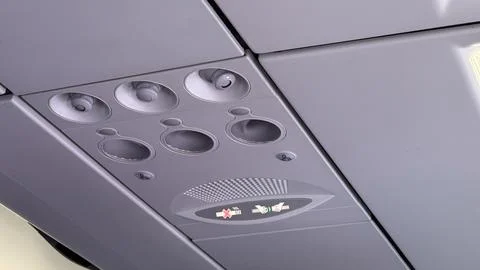 Overhead aircraft control panel showing circular vents and illuminated seat.. Stock Photos