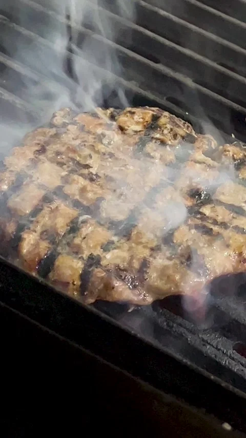 An overhead angle shows a beef patty cooking on a metal grill grate with thick, Stock Footage 309656161