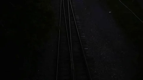Overhead birdseye view of a light rail train passing under a bridge at dusk Stock Footage 79660786