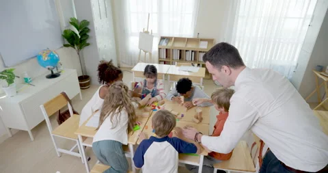 Overhead classroom view shows male teacher guiding multicultural children 스톡 동영상 337465284