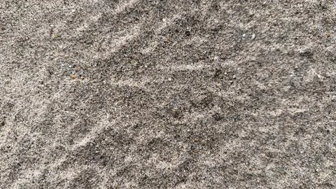 An overhead close-up captures the rough, grainy texture of gray sand, offerin Stock Photos