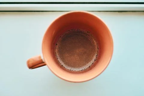 Overhead close-up of a ceramic orange mug filled with dark foamy hot coffee Stock Photos