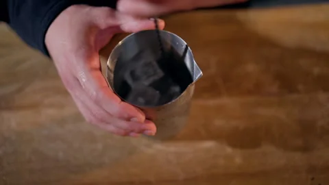 Overhead close-up of hands stirring ice cubes with a spoon in a stainless steel Stock Footage 318652283