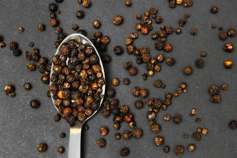 An overhead close-up of a silver spoon overflowing with whole black pepperc.. Stock Photos