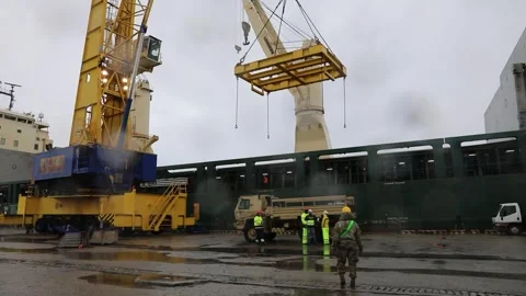 Overhead crane lowering lifting frame towards military truck at docks Stock Footage 258229768