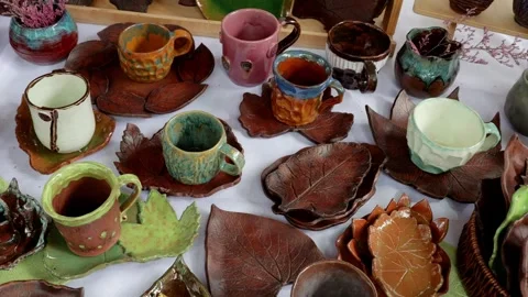 Overhead display of handcrafted glazed mugs and leaf saucers on market table Stock Footage 345955580