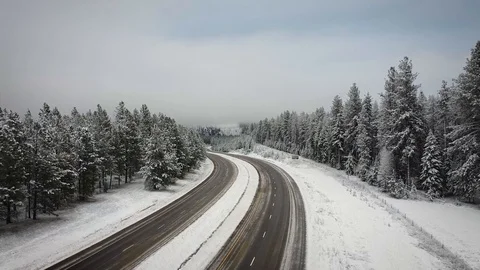 Overhead dolly shot above empty highway surrounded by snow and tall evergreen Stock Footage 125491214