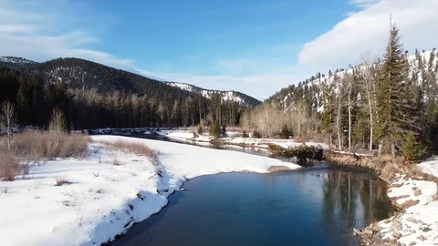 Overhead dolly shot along calm river surrounded by snow and trees toward moun Stock Footage 125401680