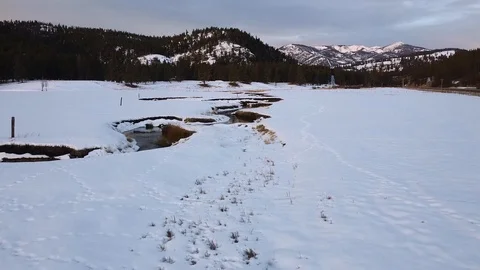 Overhead dolly shot over snow covered field with winding creek, forest and ep Stock Footage 125384594