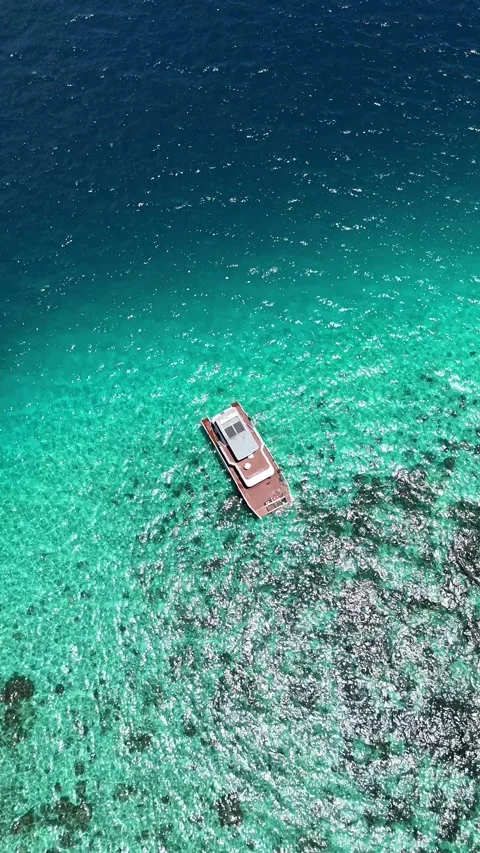 Overhead drone shot of boat floating on clear turquoise ocean Видео 332707977