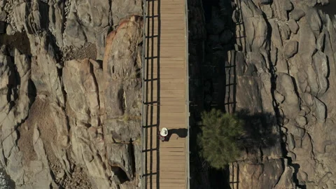 Overhead drone shot of an explorer crossing a bridge in a deserted valley 스톡 동영상 134606441