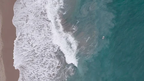 Overhead drone shot of surfer in turquoise ocean with crashing waves Stock Footage 334810201