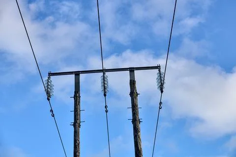 Overhead electrical power lines on old wooden pillar against the blue sky Stock Photos