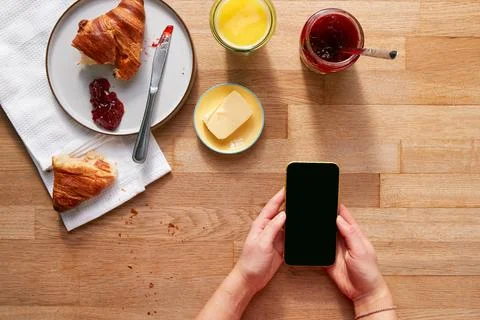 Overhead Flat Lay Of Woman Using Mobile Phone On Table Laid For Breakfast With Foto stock