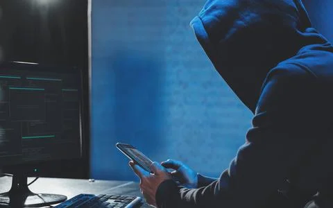 Overhead hacker in hood working at computer and mobile phone typing text in dark Stock Photos