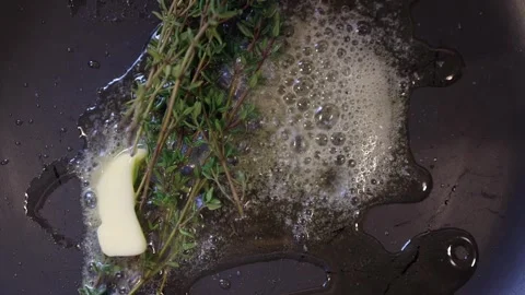 Overhead: Herb thyme and butter sizzle in hot stovetop pan, closeup Stock Footage 301489705