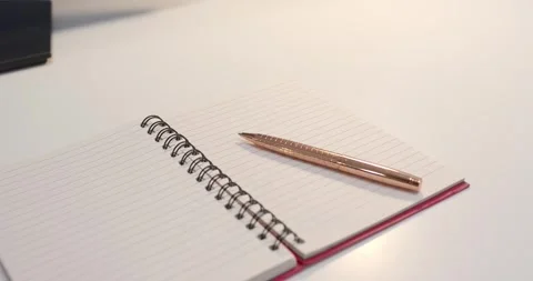 Overhead light is shifting reflections as spiral notebook with rose gold pen is Stock Footage 341026611