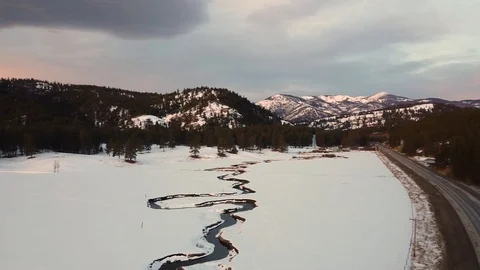 Overhead panning shot of vast snow covered pasture with winding creek, forest Stock Footage 125384607