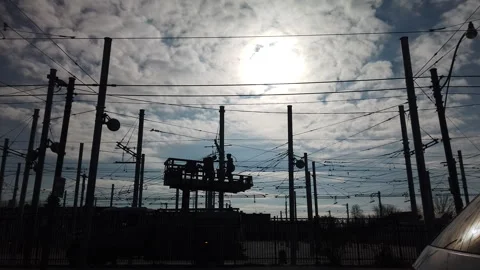 Overhead power line workers silhouetted on a raised platform connecting tram Stock Footage 322190832