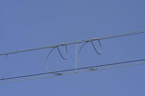 Overhead railway power lines with loop connections against a blue sky Stock Photos