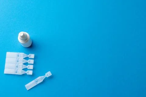 Overhead of saline solution caplets and dropper bottle on blue background with Stock Photos