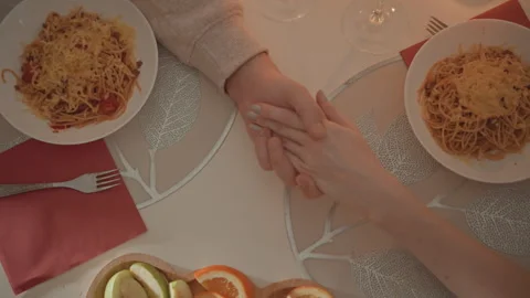 Overhead scene of two people holding hands across table with bowls of spaghetti Stock Footage 346658709