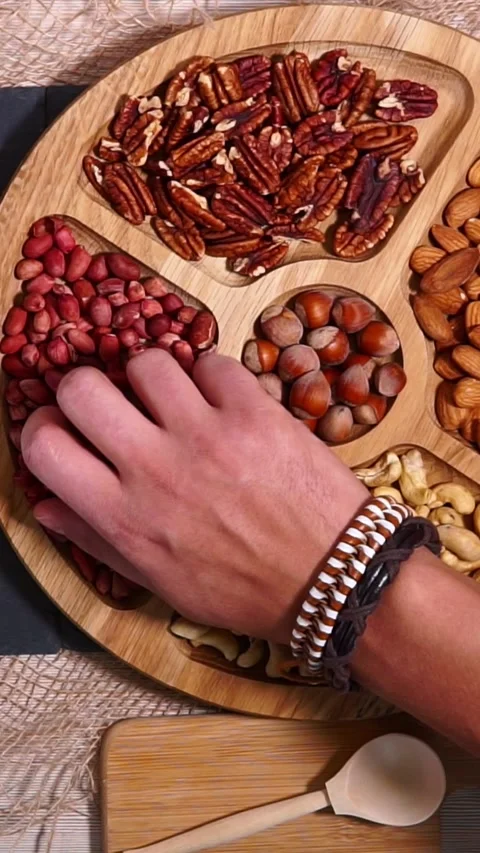 Overhead serving action with hand selecting assorted nuts from divided wooden Stock Footage 345206294