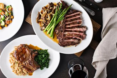 Overhead shot of a dinner table with steak and grilled pork Stock Photos