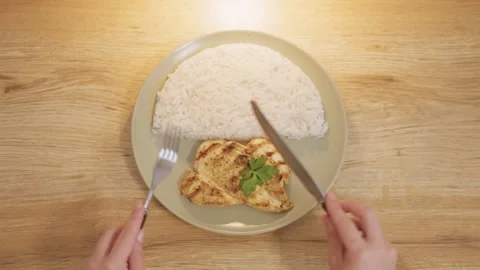 Overhead shot of hands cutting grilled chicken breast with rice on a plate Stock Footage 321193174